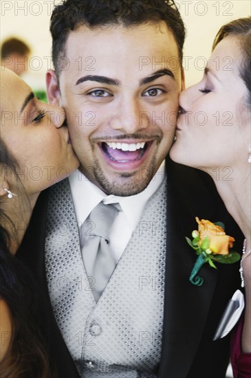 Groom being kissing by two women