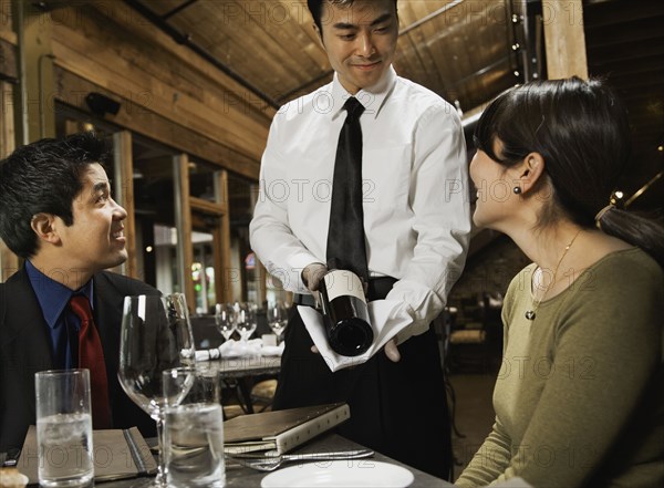 Asian waiter showing wine to couple