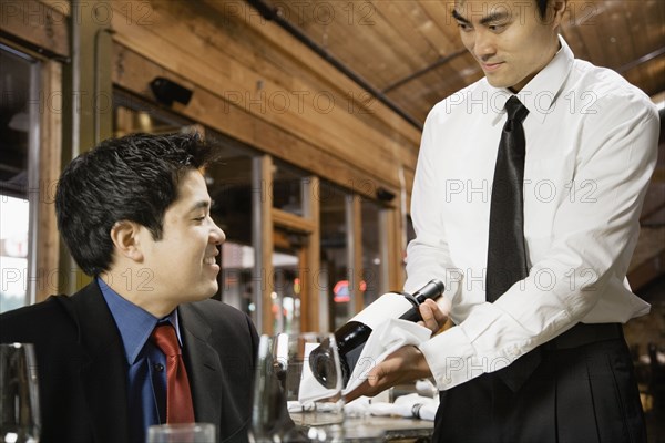 Asian waiter showing wine to customer