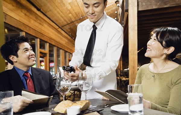 Asian waiter pouring wine for customers