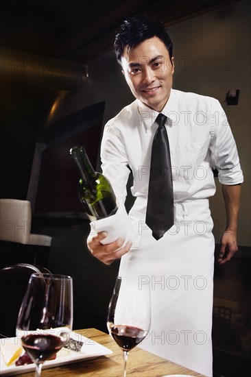 Asian waiter pouring wine