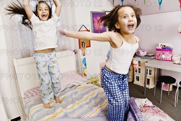 Asian sisters jumping on bed