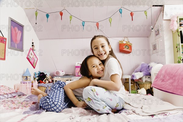 Asian sisters hugging on bed