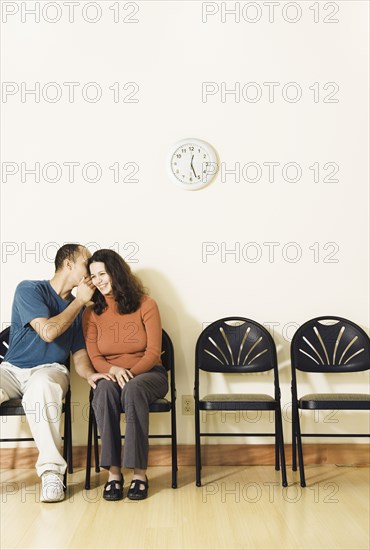 Multi-ethnic couple telling secret in waiting area