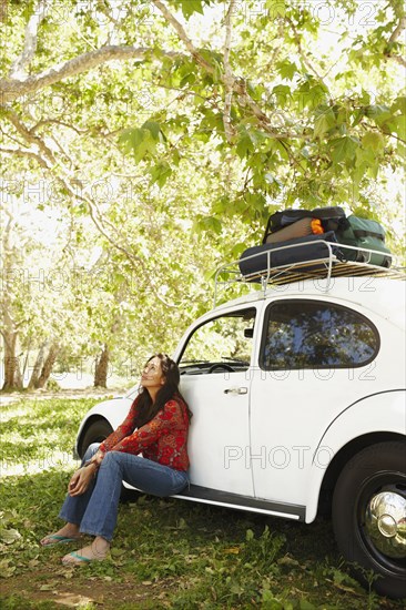 Hispanic woman sitting on side of car