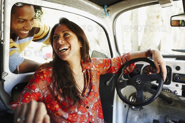 Hispanic woman sitting inside car laughing at friend