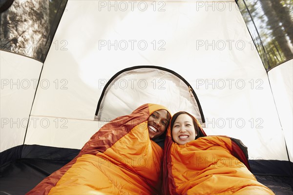 Multi-ethnic couple inside sleeping bags and tent