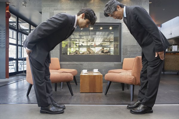 Two businessmen bowing to each other in cafe