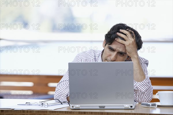 Hispanic businessman looking at laptop with hand on forehead