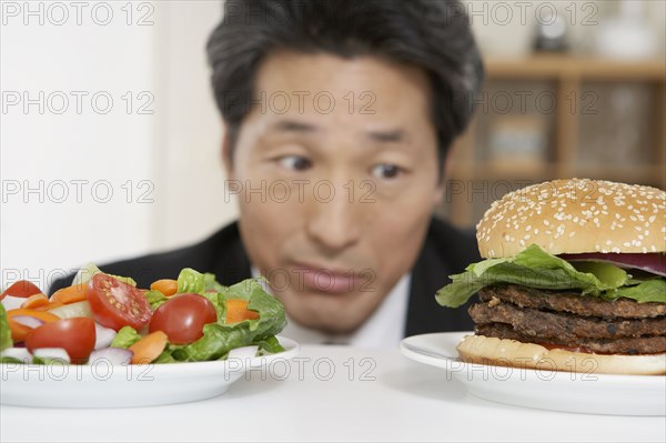Asian man looking at salad and hamburger