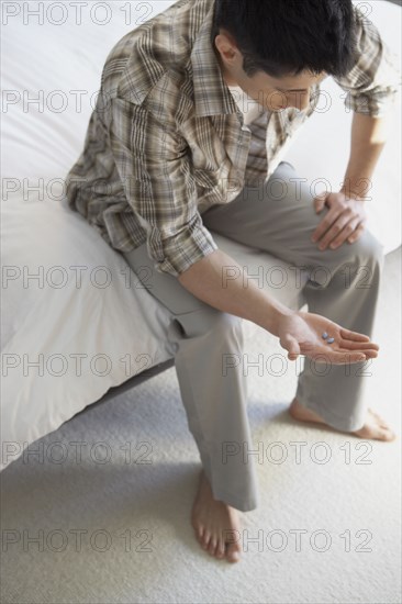 Asian man looking at pills in hand