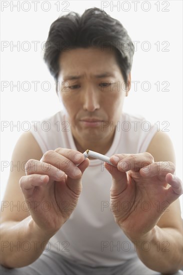 Asian man breaking cigarette in half