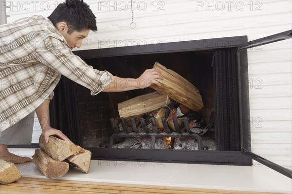 Asian man putting logs in fireplace