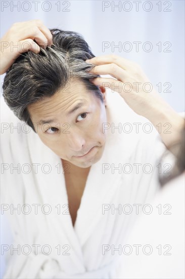 Asian man looking at gray hair in mirror