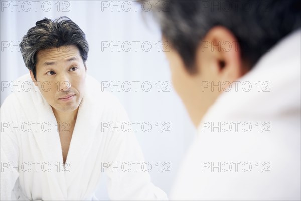 Asian man looking in bathroom mirror