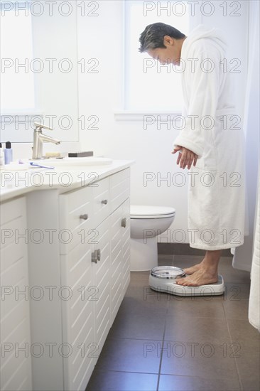 Asian man standing on bathroom scale