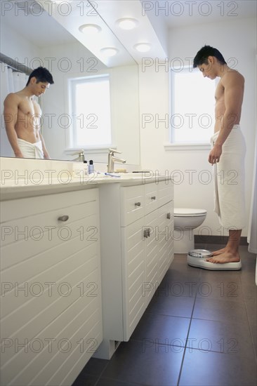 Asian man standing on bathroom scale