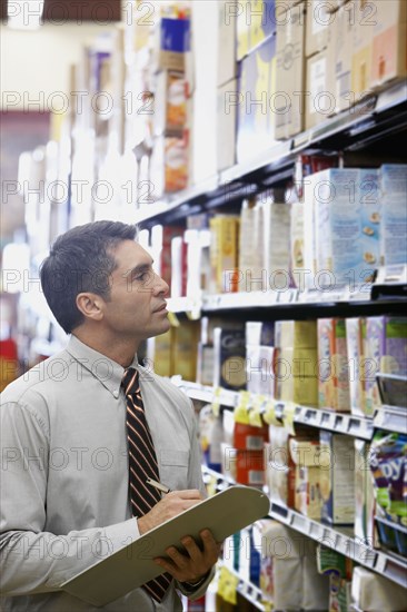 Hispanic grocery store manager writing on clipboard