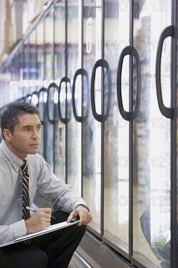 Hispanic grocery store manager writing on clipboard