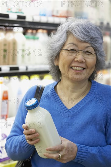 Senior Asian woman holding milk in grocery store