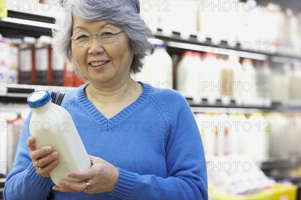 Senior Asian woman holding milk in grocery store