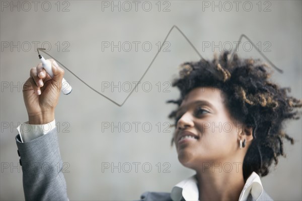 Mixed race businesswoman drawing on clear board