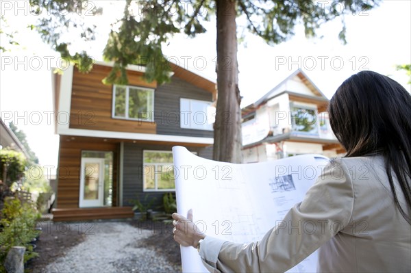 Mixed race real estate agent standing near house reviewing blueprints