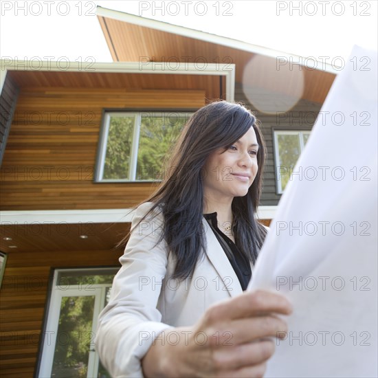 Mixed race real estate agent standing near house reviewing blueprints