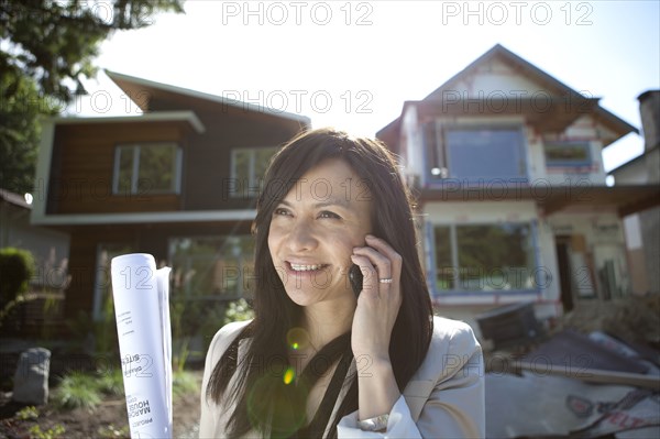 Mixed race real estate agent standing near house talking on cell phone