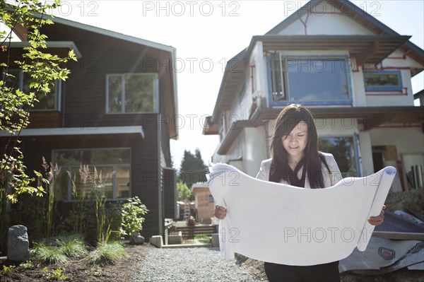 Mixed race real estate agent standing near house reviewing blueprints