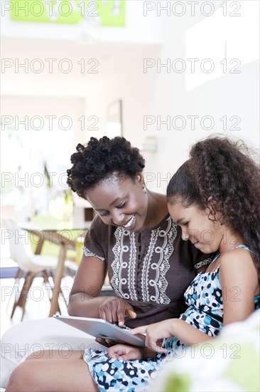 Mother and daughter using digital tablet in living room