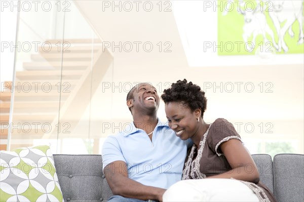 Laughing Black couple sitting on sofa in living room