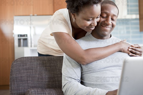 Black couple hugging and using laptop