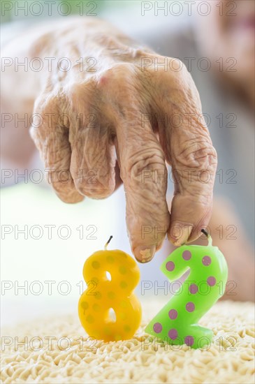 Close up of wrinkled hand holding birthday cake candle