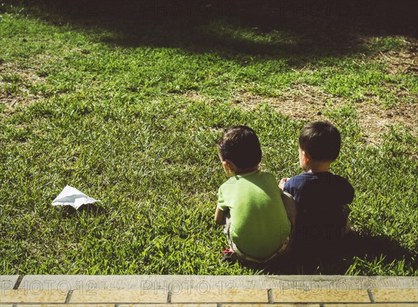 Hispanic brothers with paper airplane on lawn