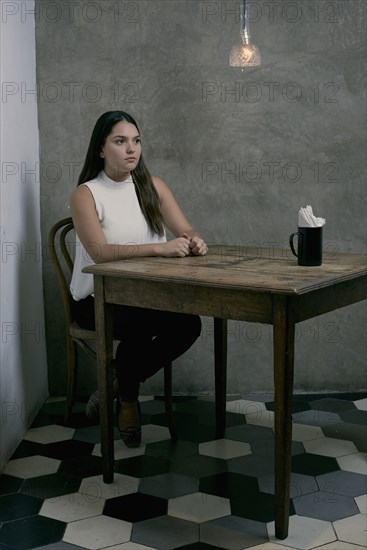 Serious Hispanic woman sitting at wooden table in corner