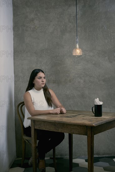 Serious Hispanic woman sitting at wooden table in corner