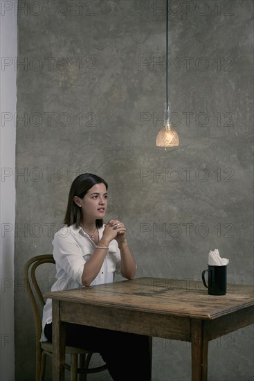 Serious Hispanic woman sitting at wooden table in corner