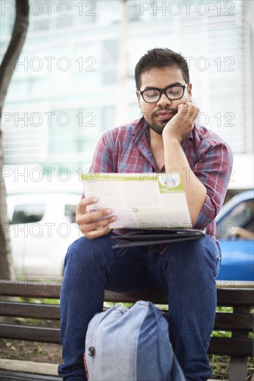 Hispanic man sitting on top of bench reading brochure