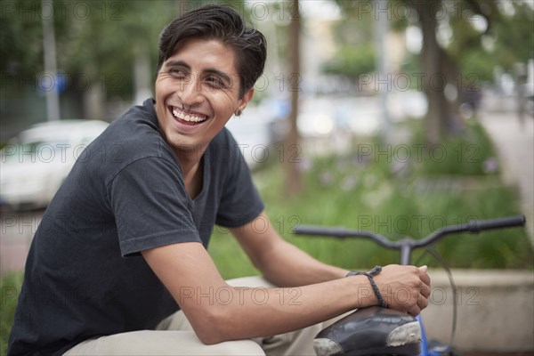 Laughing Hispanic man sitting with bicycle