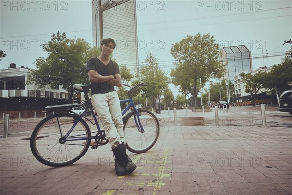 Smiling Hispanic man leaning on bicycle in city