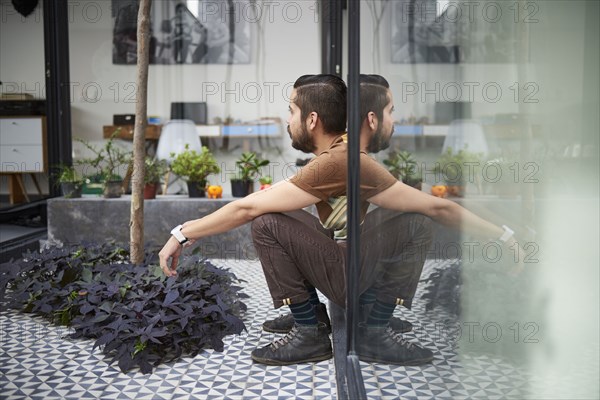 Reflection of sitting Hispanic man in atrium window