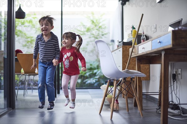 Hispanic brother and sister holding hands and jumping