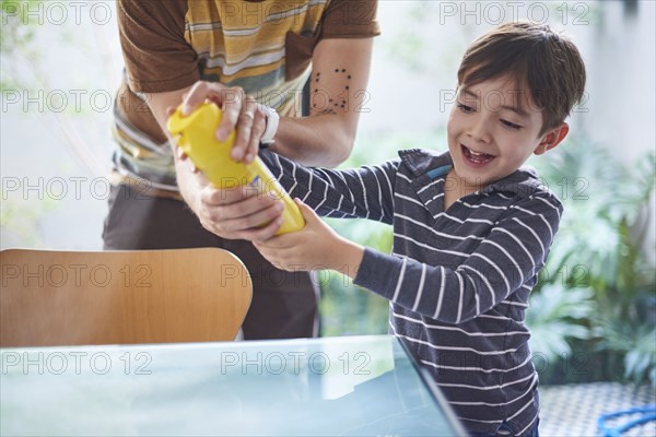 Hispanic boy helping father spray cleaner on table