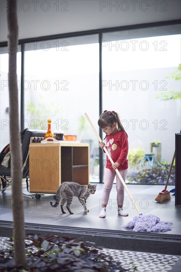 Hispanic girl watching cat and mopping floor