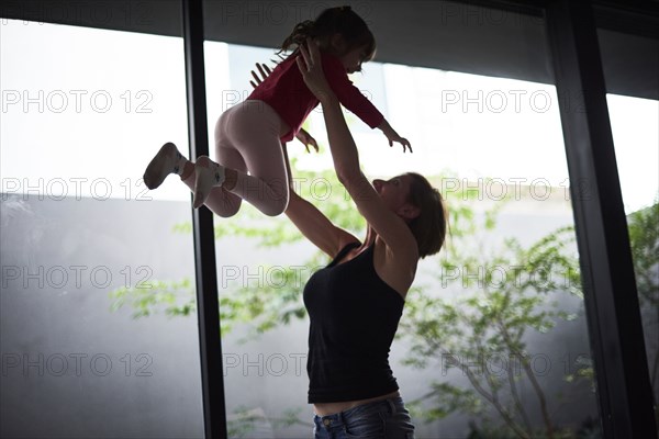 Playful Hispanic mother lifting daughter