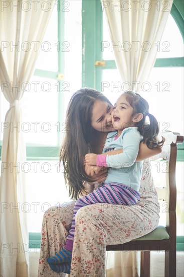 Hispanic mother sitting in chair holding laughing daughter