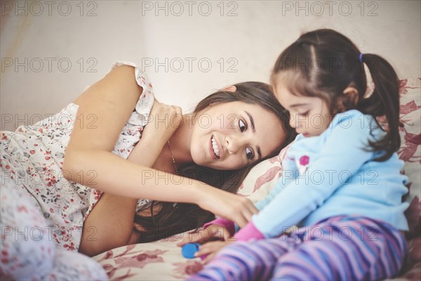 Hispanic mother playing with daughter on bed