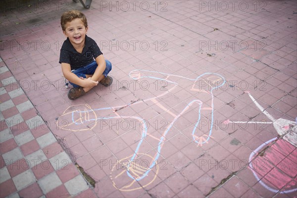 Hispanic boy with chalk drawing on sidewalk