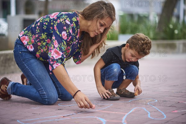 Hispanic mother and son drawing on sidewalk with chalk